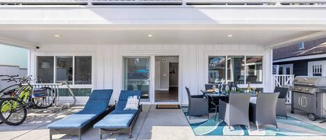 A covered outdoor patio with lounge chairs, a dining table, and a grill.