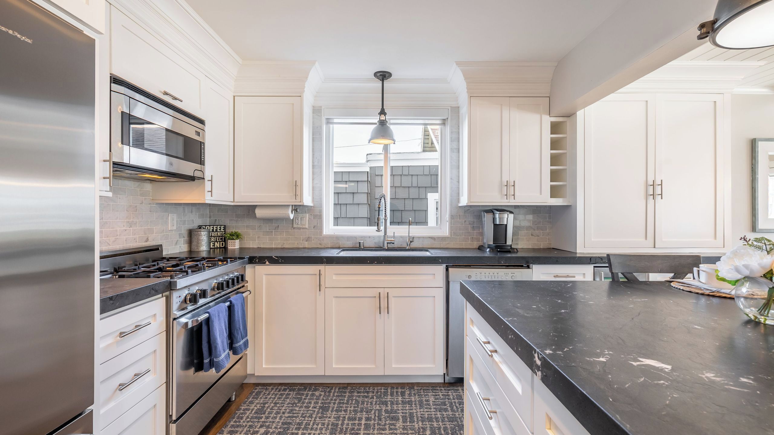 A modern kitchen with white cabinetry, a stainless steel range, and a black countertop.