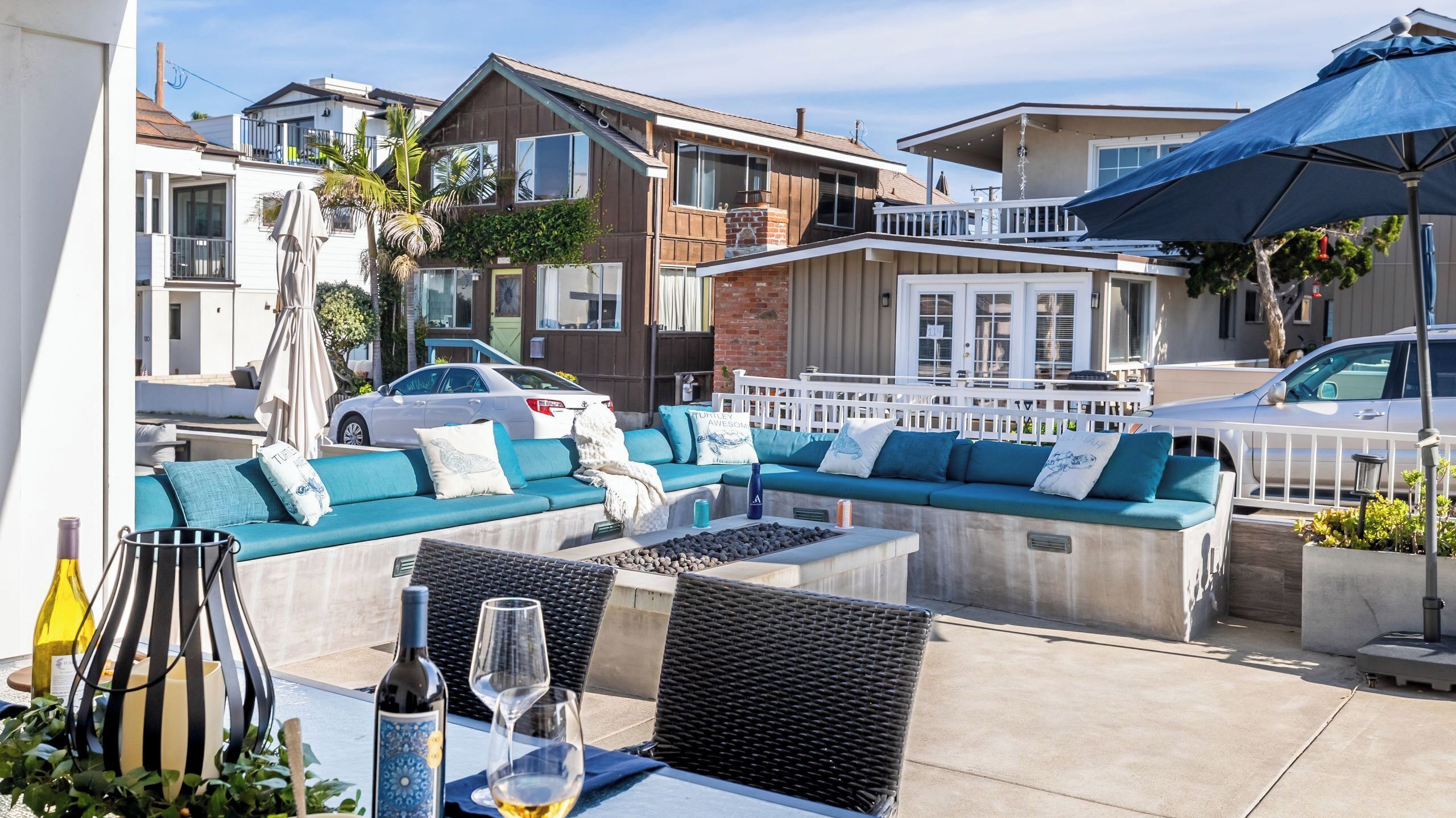 A patio with outdoor seating, a table with wine glasses and bottles, and a car parked nearby.