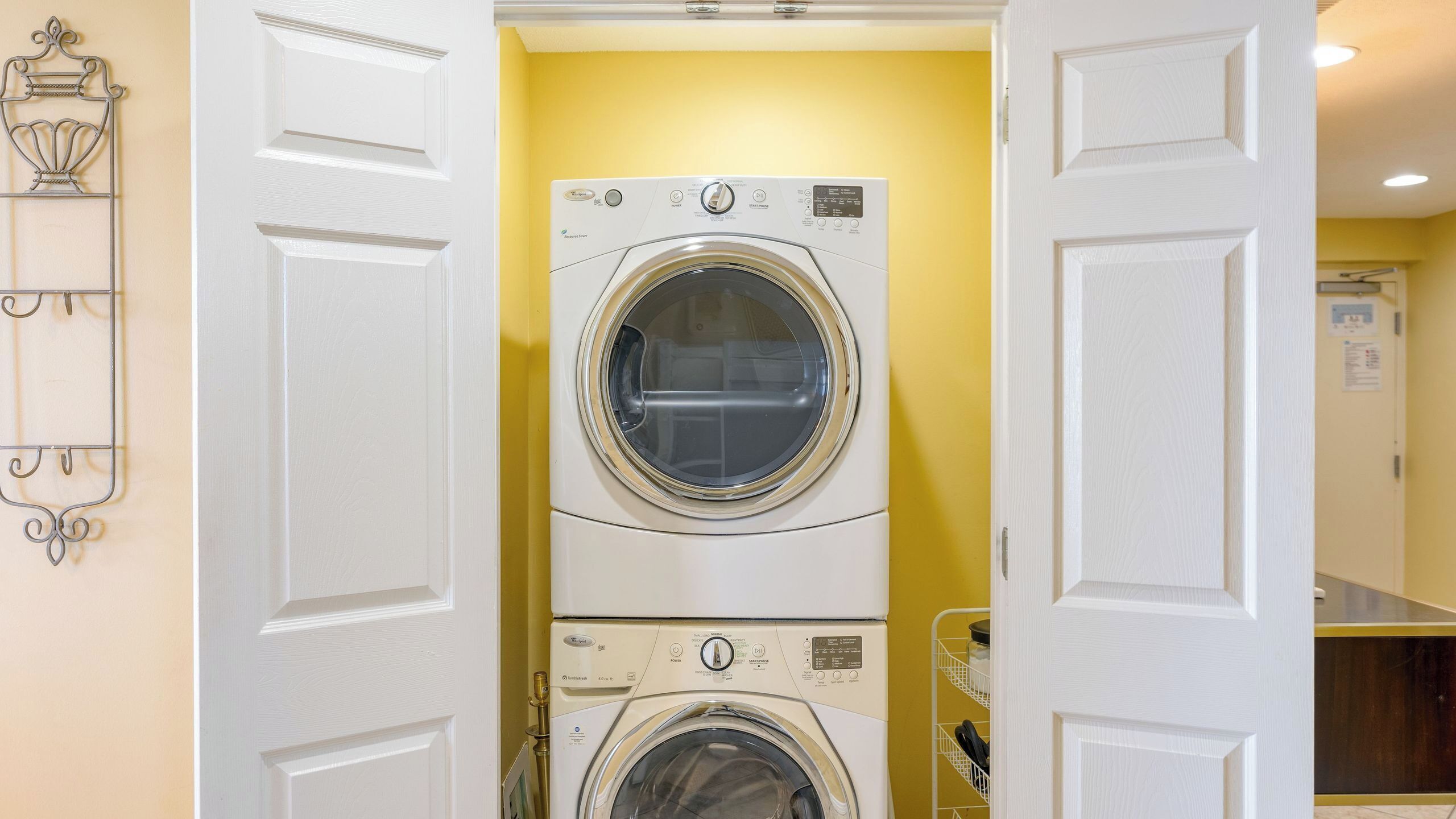 Un cuarto de lavandería con dos lavadoras y secadoras apiladas, puertas blancas y una pared amarilla.