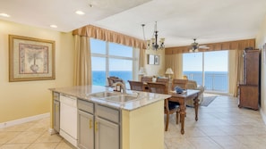 A kitchen with a large island, a dining area with a view of the ocean, and a living room with a view of the ocean.