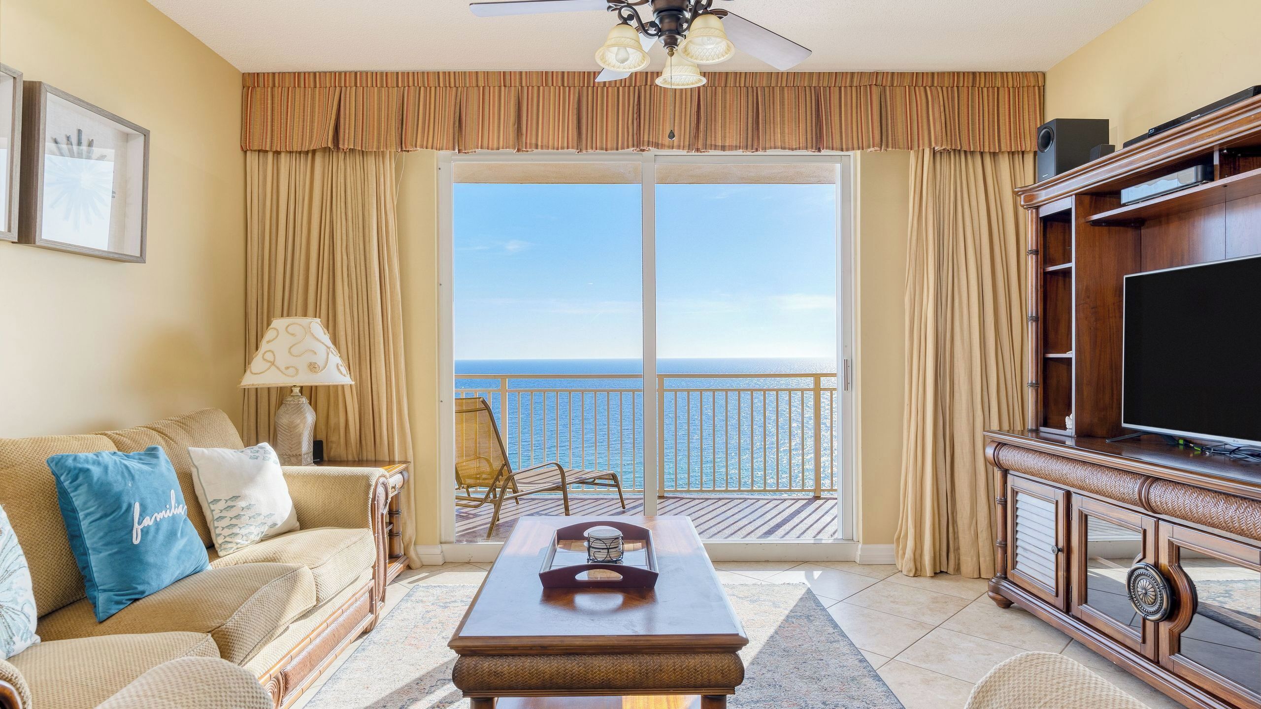 A room with a sofa, a coffee table, a TV, and a balcony with a view of the sea.