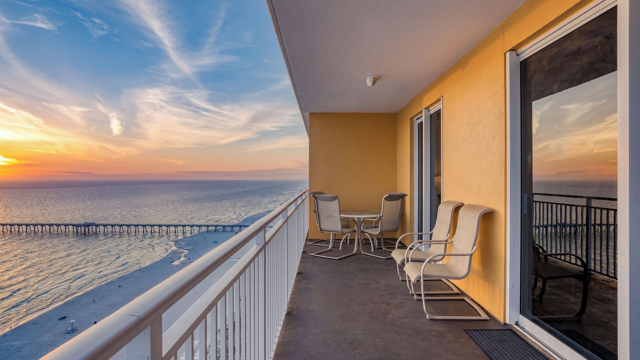 A balcony with a view of the ocean and a pier, furnished with chairs and a table.