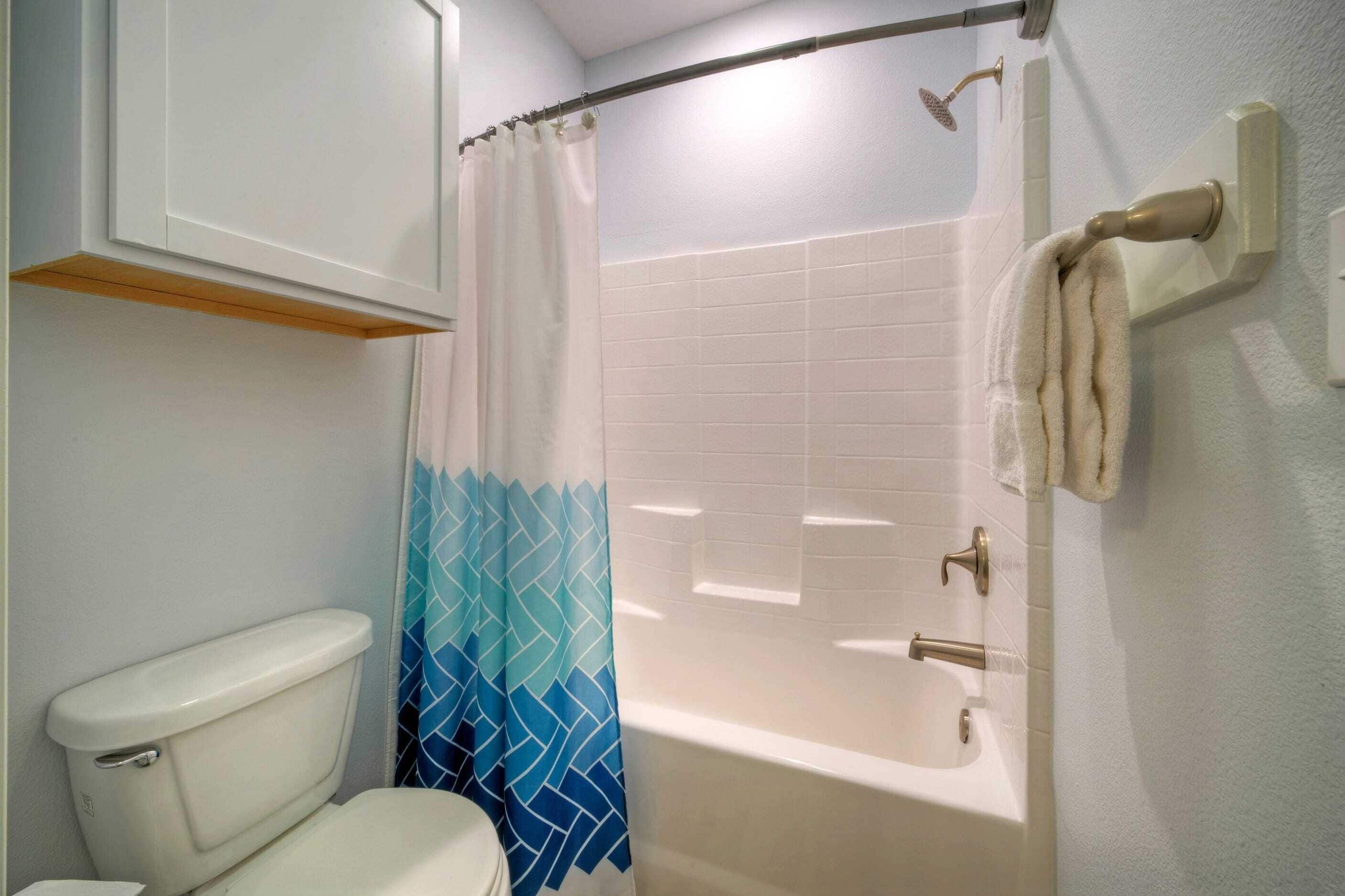 A bathroom with a toilet, a shower with a curtain, and a bathtub.