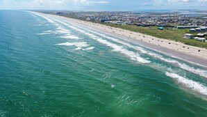 Luchtbeeld van een kuststad met een lang strand, heldere lucht en een mix van woon- en bedrijfsgebouwen.