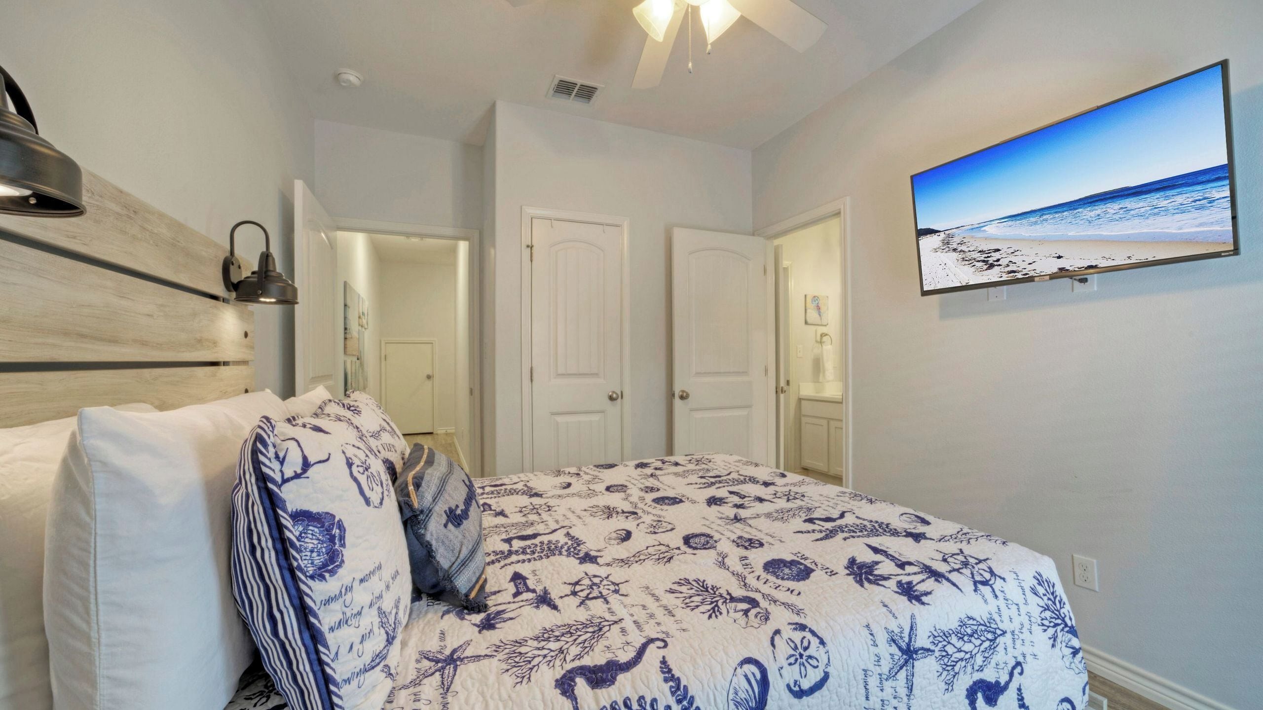 A bedroom with a bed, a wall-mounted TV, and a ceiling fan.
