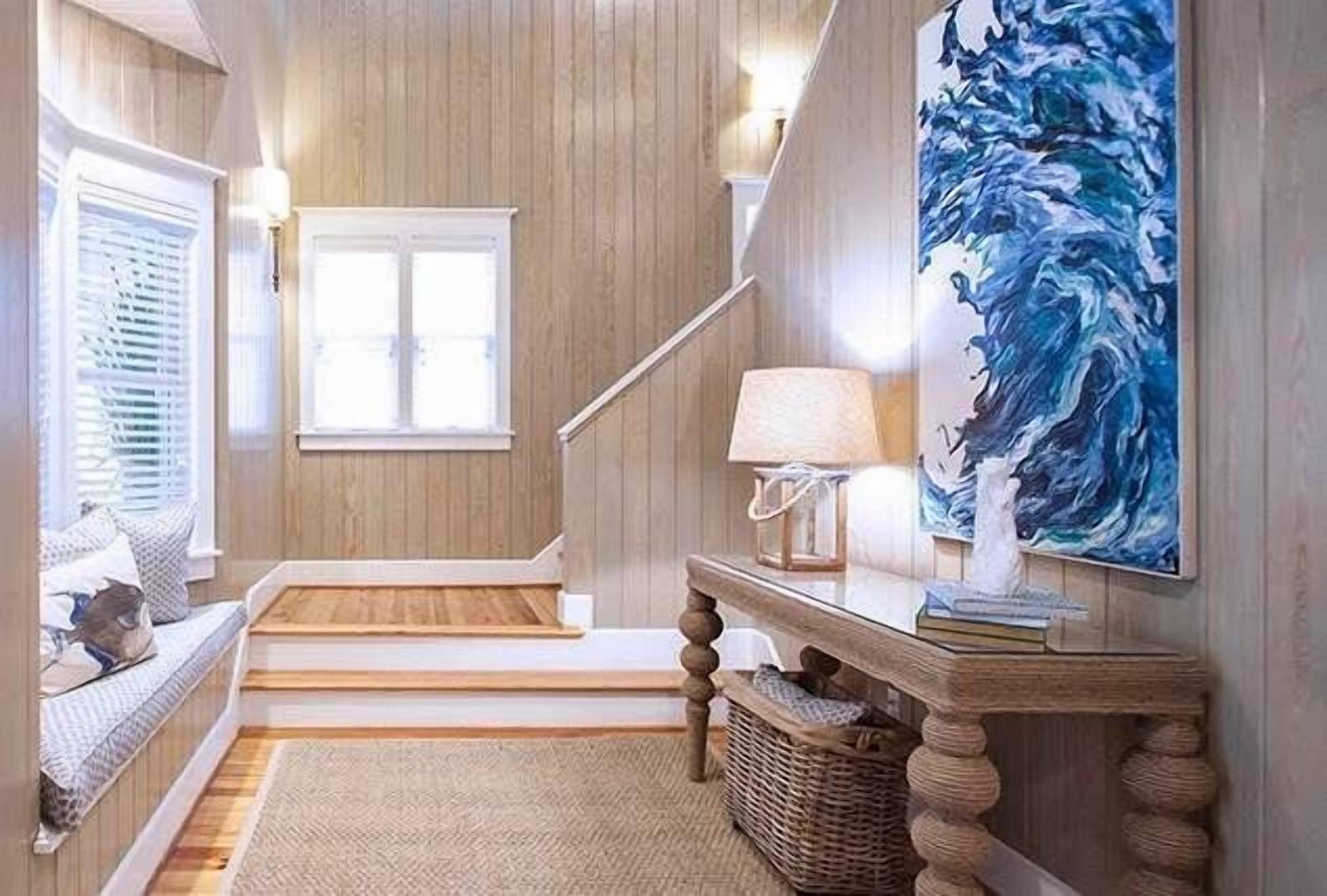 Una escalera conduce a un rellano con vistas al exterior, una lámpara de pared y un cuadro abstracto de gran tamaño.