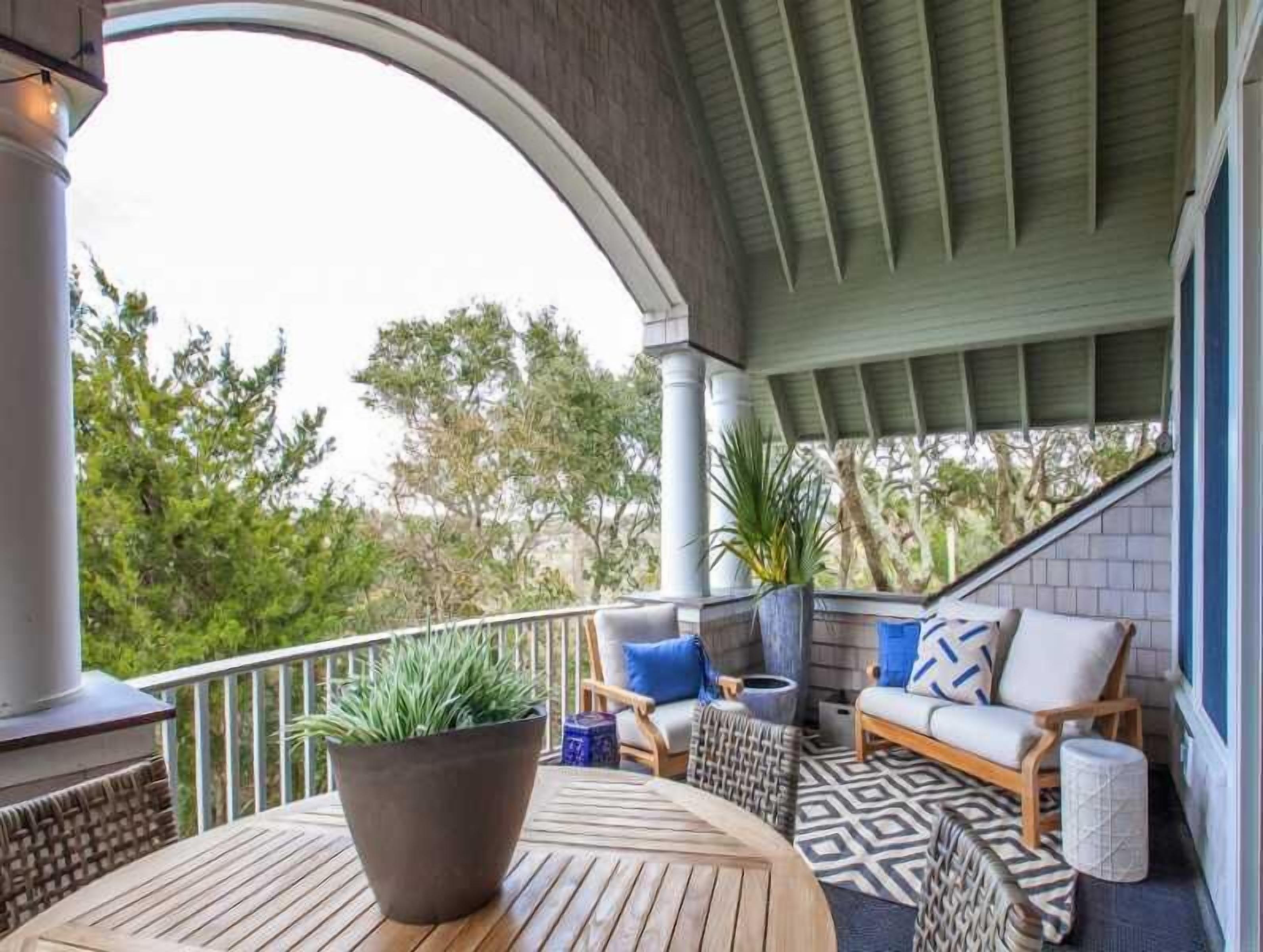 A covered outdoor seating area with a wooden table, chairs, and a potted plant.