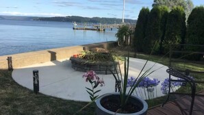 A deck with a potted plant, a bench, and a view of a body of water with a dock in the background. - Waterfront Hoodsport Cabin, Hood Canal Beach Oasis (Shelton)