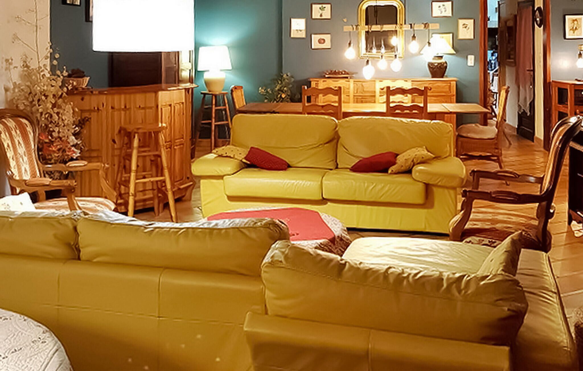 Un salon avec un canapé jaune, des chaises en bois, un buffet en bois et une table à manger.