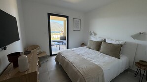 Une chambre avec un grand lit, une télévision, un bureau et une chaise. Elle dispose d’un balcon avec vue sur une montagne.