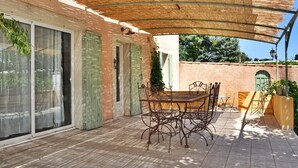 Une terrasse extérieure avec une table et des chaises, un espace abrité avec un toit de chaume et un mur en briques.