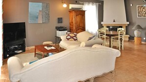 Un salon comprenant un canapé, un téléviseur, une table à manger avec des chaises, une cheminée et une lampe.