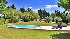 Une piscine rectangulaire entourée d’une terrasse, avec une pelouse verdoyante et une rangée de chaises longues.