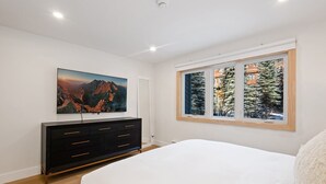 A bedroom with a bed, a dresser, a painting, and a window with a view of trees. - Riverside Getaway | Walk to Main St, Festival & Ski Fun (Telluride)
