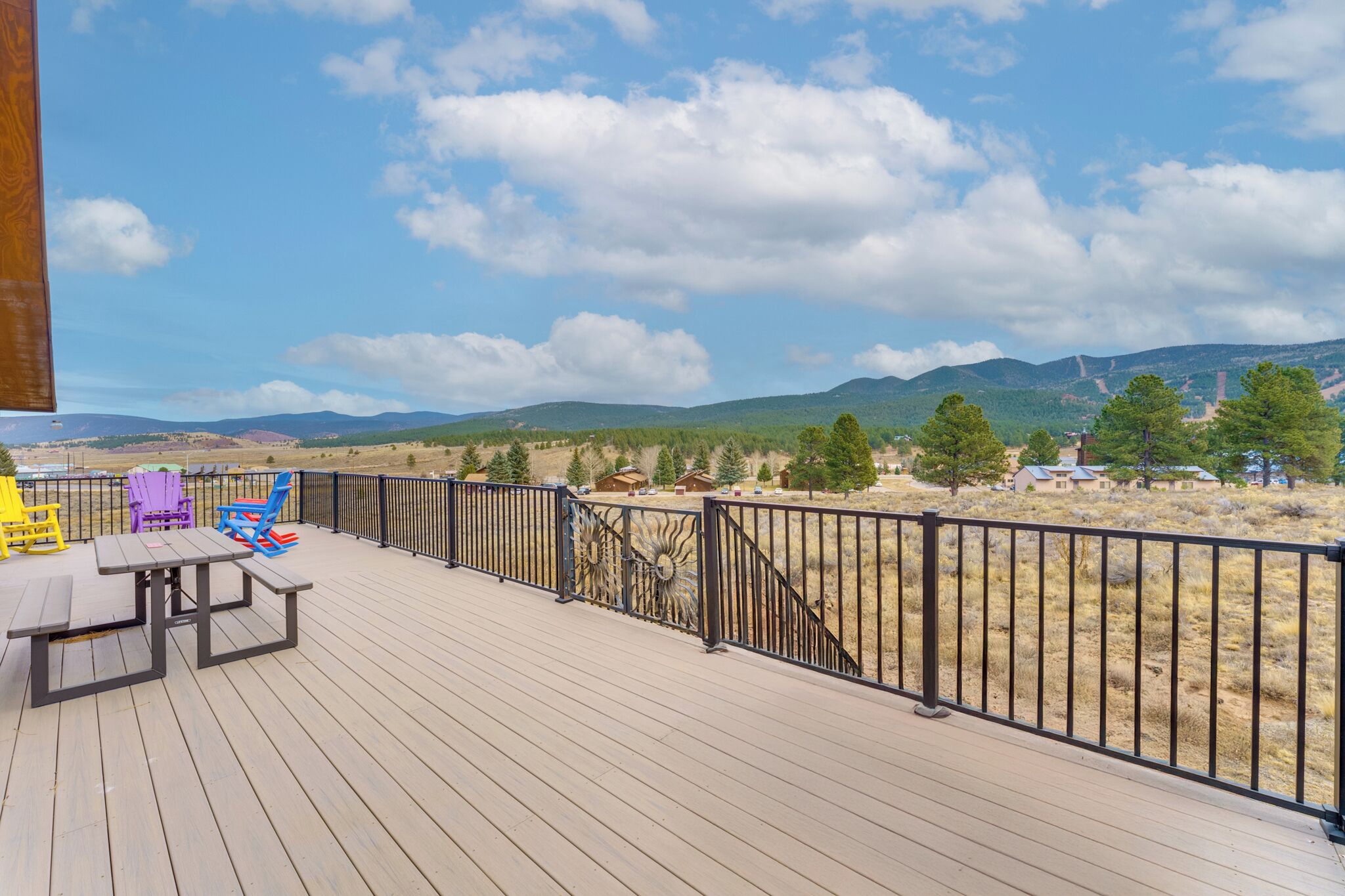 Una terraza de madera con una mesa de picnic y sillas Adirondack de colores, con vistas a un paisaje montañoso.