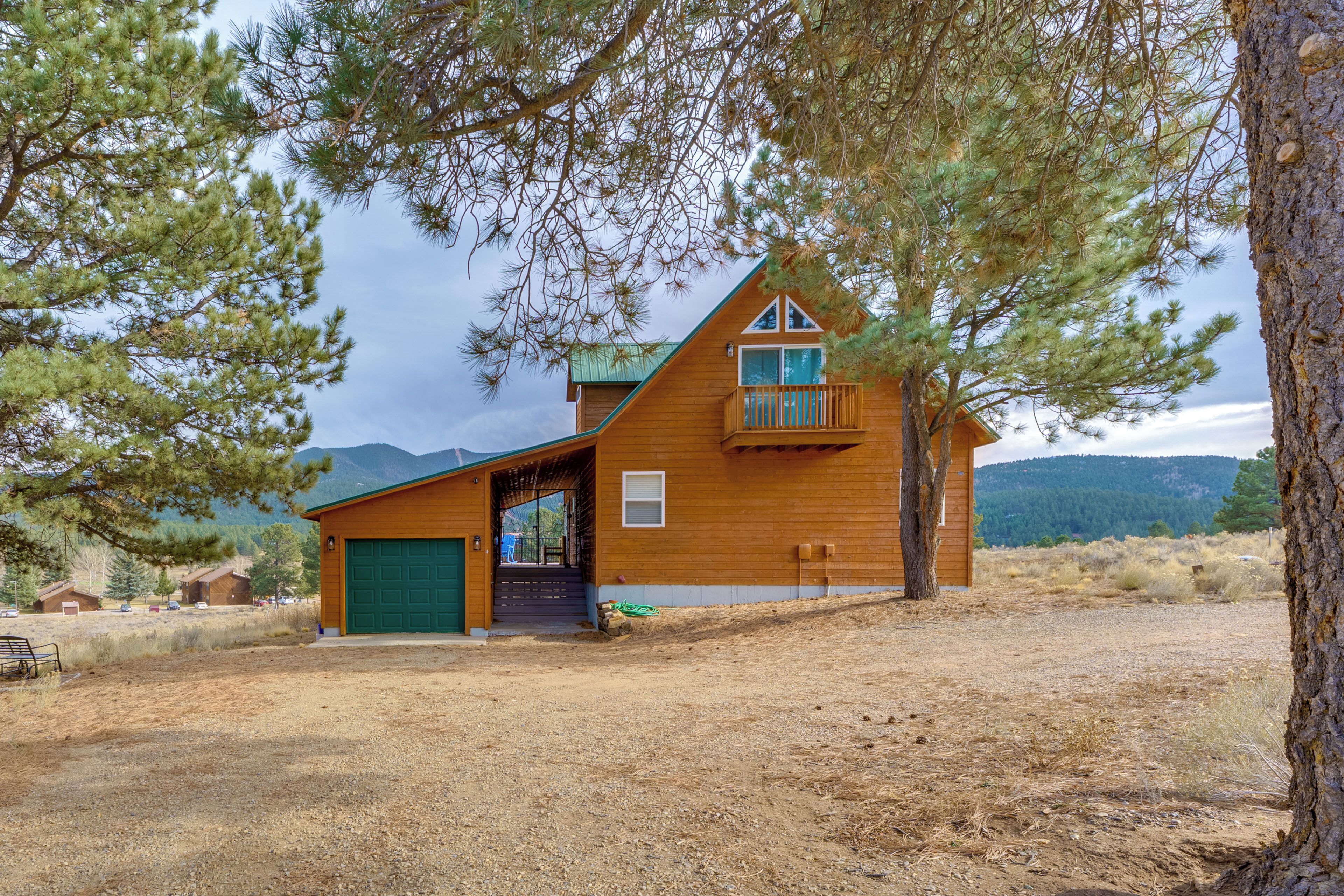 A wooden cabin with a green garage door, a balcony, and a mountain backdrop.