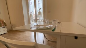A dining area with a white table, chairs, and a window with curtains. - Colorful NoLo Studio (Milano)