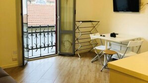 A room with a sliding glass door, a small table with chairs, a TV mounted on the wall, and a window with a view of buildings. - Colorful NoLo Studio (Milano)