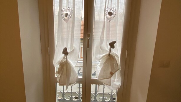 A view through a window with white curtains featuring heart patterns and a balcony railing. - Colorful NoLo Studio (Milano)