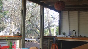 Een rustiek blokhutinterieur met een houten tafel, een hoed, een groene fles en een raam met uitzicht op een bos.