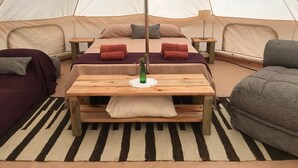 Een gezellig tentverblijf met een centraal bed, twee nachtkastjes, een houten bank en een grijze slaapbank.