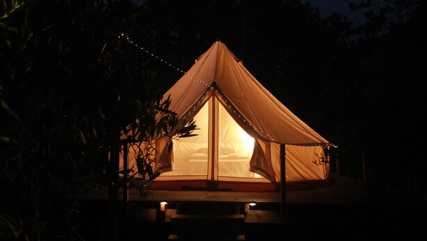 Een tent met een centrale ingang, omringd door een houten terras, verlicht met lichtslingers.