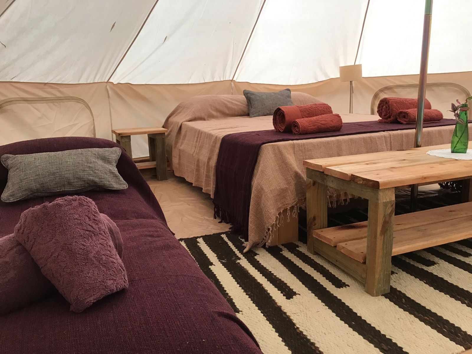 A tent with two beds, a wooden table, and a striped rug.