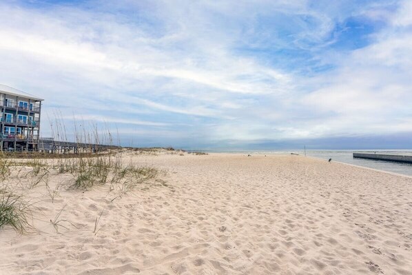 A beach with a building on the left, clear skies, and a calm sea.