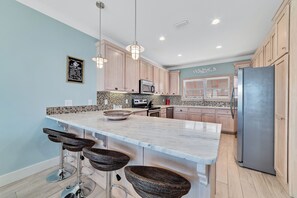 A kitchen with a large island, bar stools, wooden cabinets, a refrigerator, and a microwave.