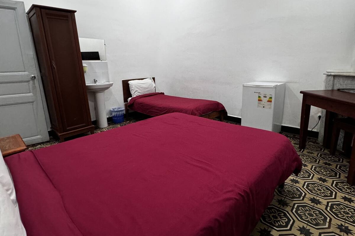 A hotel room with two beds, a wardrobe, a sink, and a refrigerator.