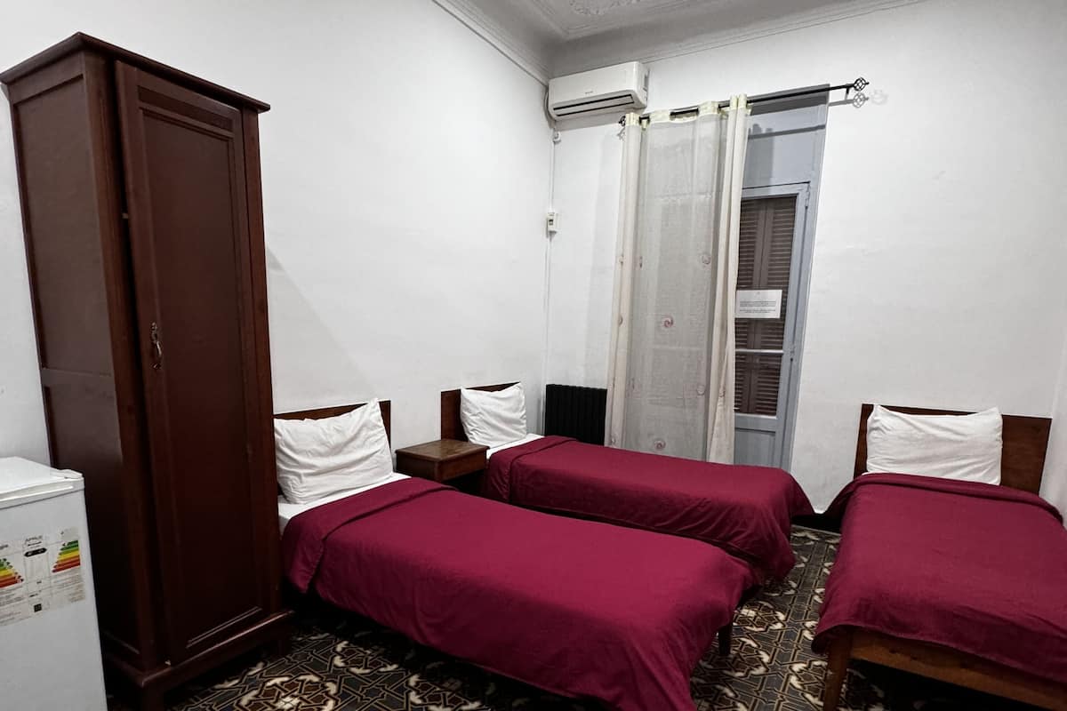 A hotel room with two beds, a wardrobe, a small table, and a patterned floor.