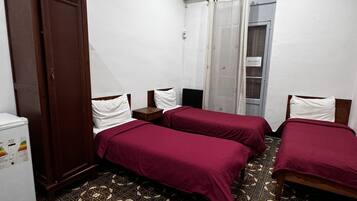 Habitación de hotel con dos camas, un armario, una mesita pequeña y suelo estampado.