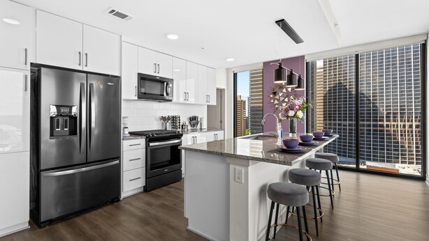 A modern kitchen with a large island, stainless steel appliances, and a city view through large windows. - The Velvet Room | 17th Floor Luxury Condo | Skyline Views & Balcony (Atlanta)