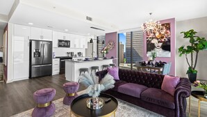 A modern kitchen with stainless steel appliances, a dining area with a purple sofa, and a large window. - The Velvet Room | 17th Floor Luxury Condo | Skyline Views & Balcony (Atlanta)