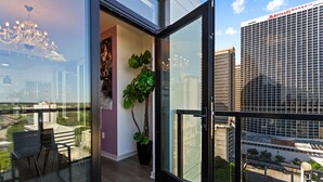 A modern hotel room with a glass door, a potted plant, a chandelier, and a view of the Marriott Marquis building. - The Velvet Room | 17th Floor Luxury Condo | Skyline Views & Balcony (Atlanta)