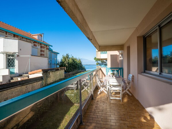 A balcony with a view of the sea, a table with chairs, and a window.