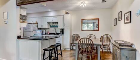 A kitchen with white cabinets, a central island with stools, and a dining area with wooden chairs and a table.
