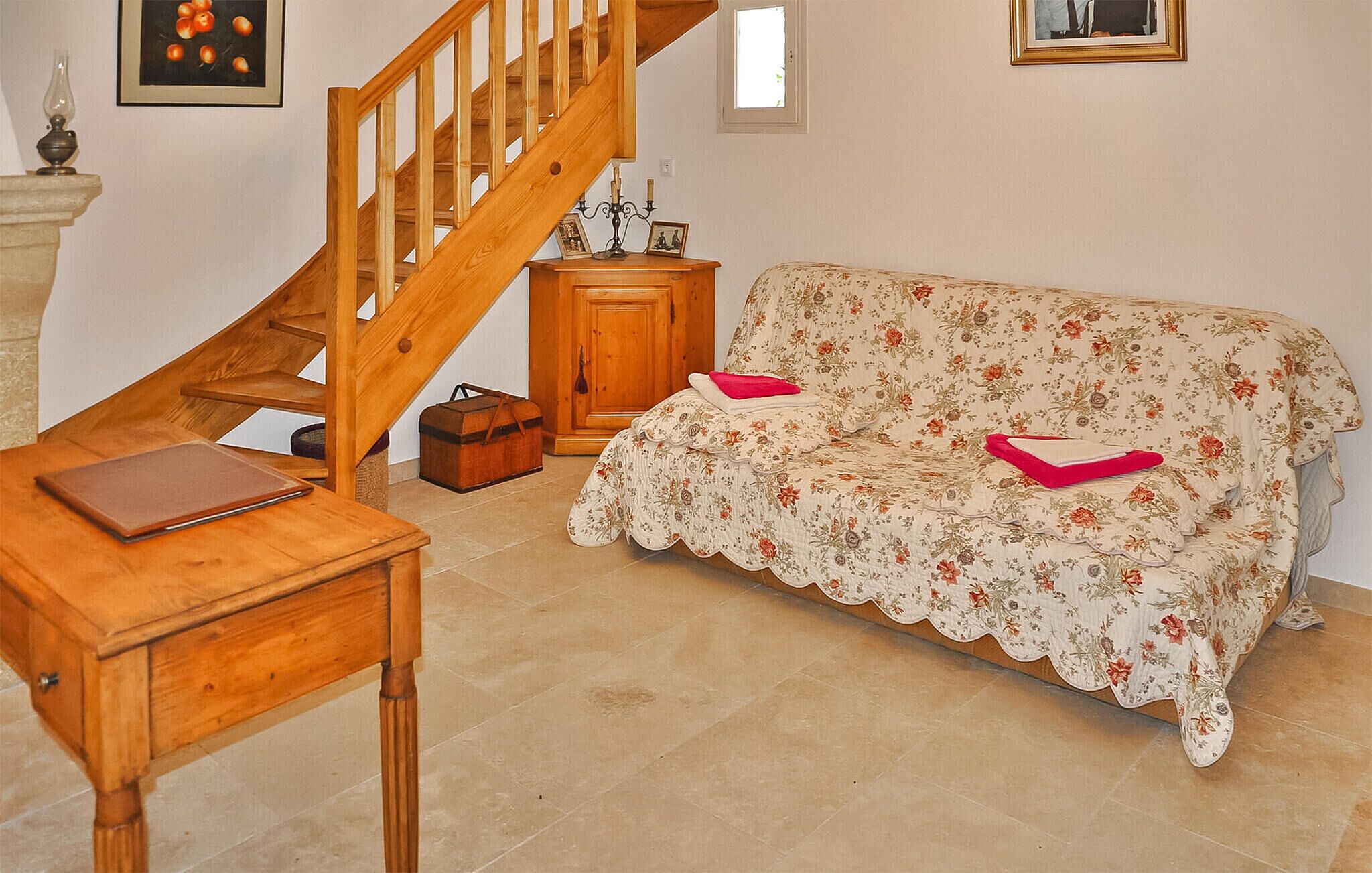Un escalier en bois, une table en bois avec un livre, un canapé à motifs floraux avec des coussins et une armoire en bois.