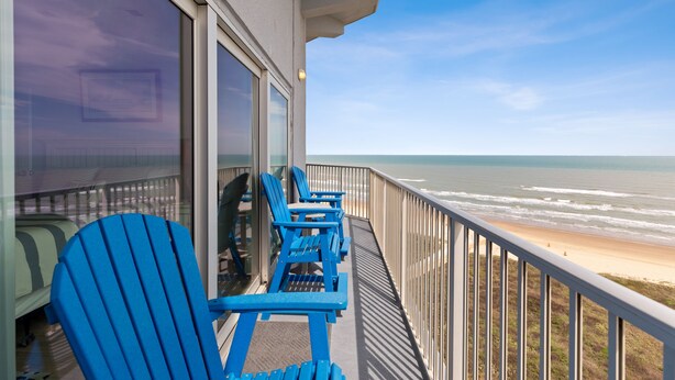 Un balcón con sillas Adirondack azules con vista a la playa.