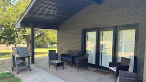 Un patio couvert comprenant un barbecue, des meubles en osier et un mur en briques.