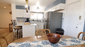Une cuisine moderne avec des meubles blancs, un réfrigérateur en acier inoxydable et un coin repas comprenant une table et des chaises en bois.