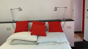 A bed with white and red pillows, two desk lamps, and a shelf with red bottles. - Medieval Mountain Oasis With a Private G (Castelbianco)