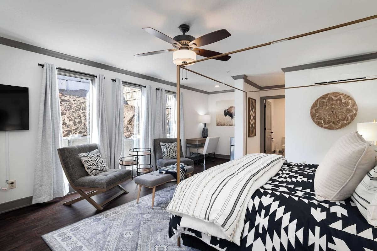 A modern bedroom with a bed, a desk, a chair, and a ceiling fan.
