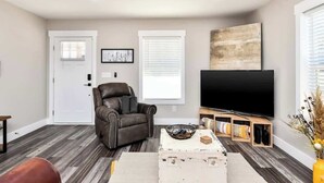 A living room with a leather chair, a white coffee table, a flat-screen TV on a wooden stand, and a door with a window.