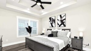 A bedroom with a bed, bedside tables, a ceiling fan, and abstract wall art.