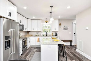 A modern kitchen with white cabinets, stainless steel appliances, and a central island with stools. - Modern Urban Retreat in Downtown Greenville (Greenville)
