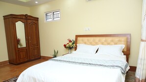 Un dormitorio con cama, armario, ventana y un florero con flores.