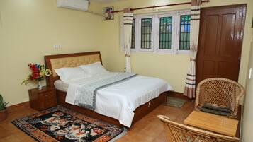 Um quarto com cama, mesa de cabeceira, cadeira, janela com grades e porta.