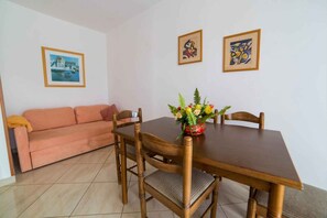 Uma sala de jantar com mesa de madeira, quatro cadeiras, um sofá e um vaso de flores.